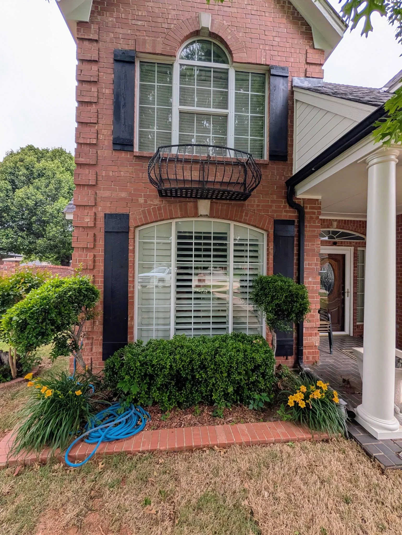 Red brick home with arched window, black shutters, and plantation shutters installed