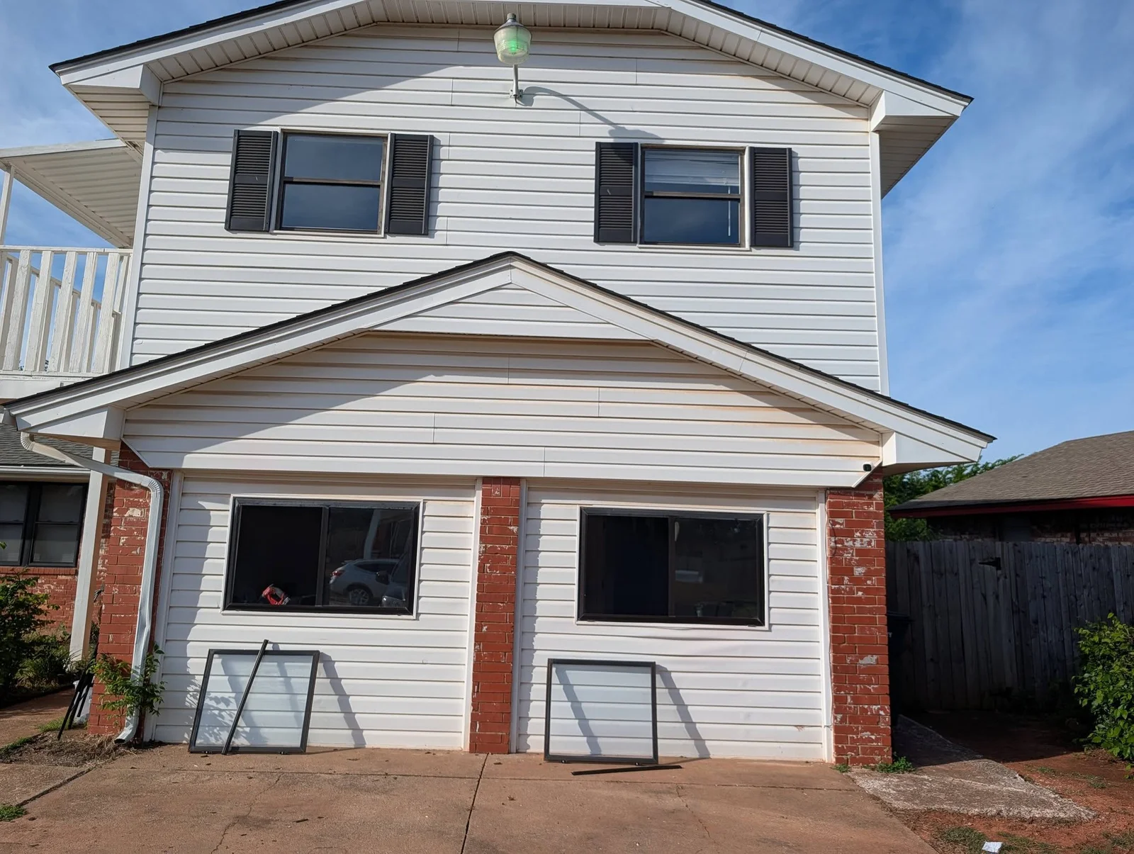 Black-framed windows installed on white vinyl siding with red brick trim, two-story residential home